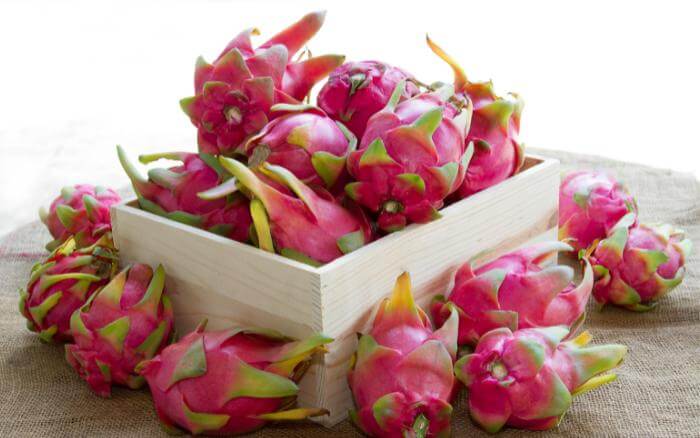 Pitaya em lote, dentro e ao redor de caixote de madeira.