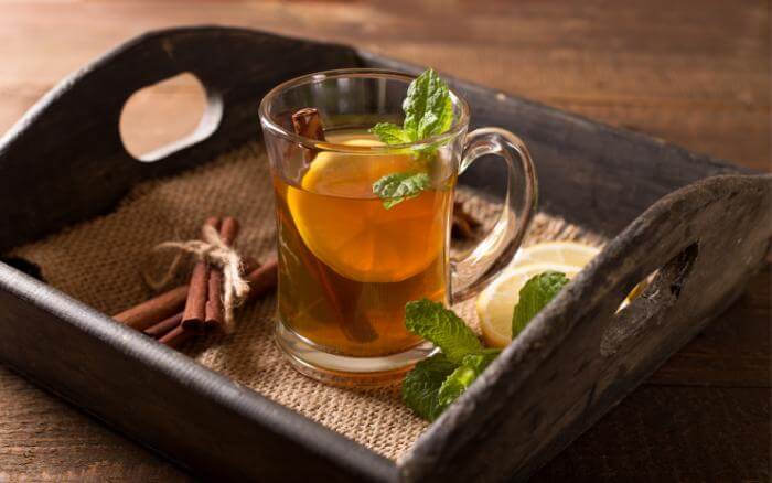 Ervas-que-combatem-os-sintomas-da-TPM Chá de ervas em xícara, sobre bandeja de madeira.